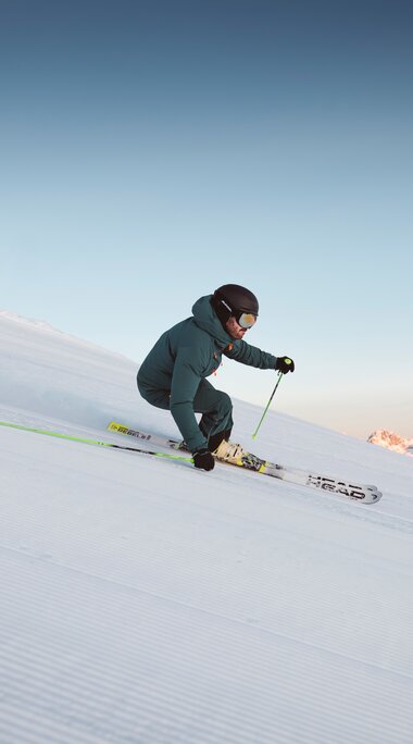 Skifahrer auf präparierter Piste in den Alpen bei Sonnenaufgang, Blick auf verschneite Berge