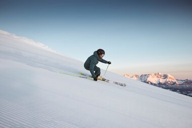 Skifahrer auf präparierter Piste in den Alpen bei Sonnenaufgang, Blick auf verschneite Berge
