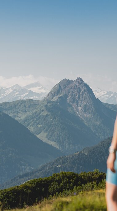 Zwei Wandernde stehen auf einer Bergwiese und blicken in die Alpenlandschaft im Brixental.