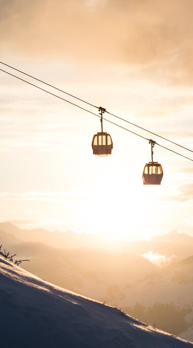 Winterseilbahn über verschneitem Berg mit Abendsonne und Wolken im Hintergrund
