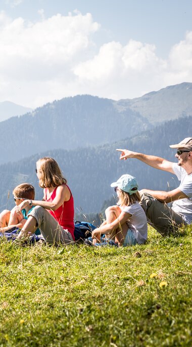 Familie beim Wandern auf einer Almwiese mit Blick auf die Berge in den Kitzbüheler Alpen