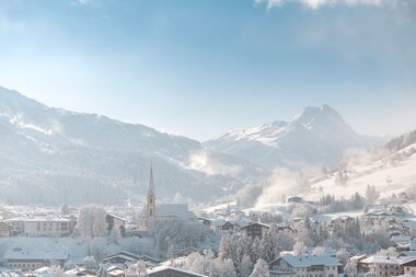 Die Kirche von Kirchberg in Tirol liegt eingebettet in eine verschneite Winterlandschaft.