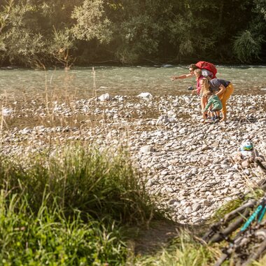 Familie erkundet das Ufer der Großache am Flusserlebnisweg Achendamm in Kirchdorf in Tirol und beobachtet das Wasser zwischen den Kiesbänken